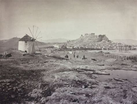 An Old Black And White Photo Of People On A Dirt Field With Windmills