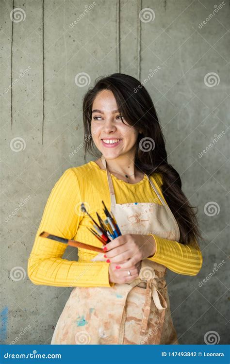 Young Beautiful Lady Artist In Apron With Paint Stains In Her Loft