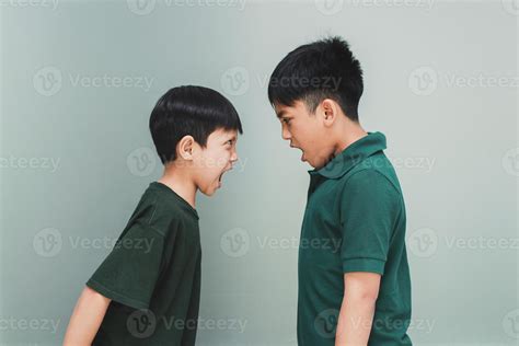 Two angry siblings looking each other and shouting each other on grey