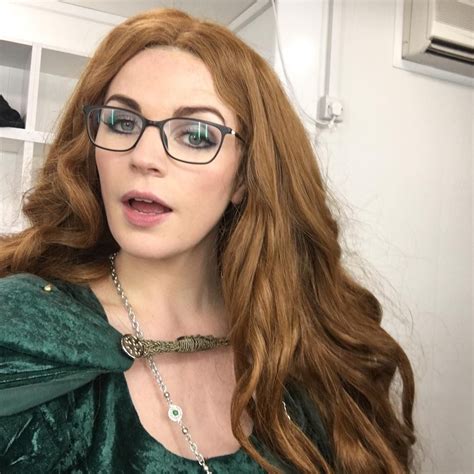A Woman With Long Red Hair Wearing Glasses And A Green Dress Is Looking