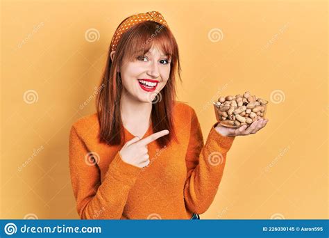 Redhead Young Woman Holding Peanuts Smiling Happy Pointing With Hand