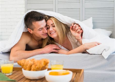 Junger Mann Der Nette Frau Im Bett Unter Decke Nahe Lebensmittel Auf Frühstückstische Umarmt