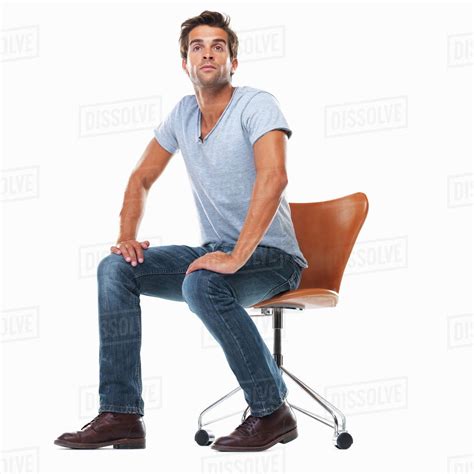Studio Shot Of Young Man Sitting On Chair With Hands On