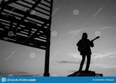 Silhouette Of A Statue Playing Guitar Near A Structure Stock Photo