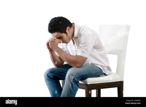 A Young Indian Man Sitting On A White Chair Holding His Head In His
