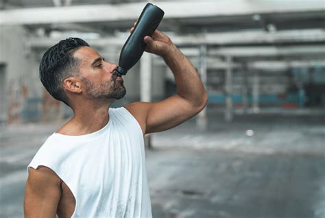 Athletic Man Drinking Water After Exercising In A Warehouse Stock Photo