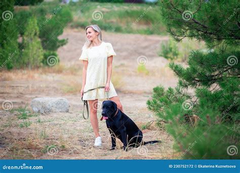eine schöne junge frau in einem kleid spaziert mit ihrem hund in einem stadtpark oder im wald