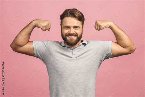 Waist Up Portrait Of Muscular Young Man Flexing His Biceps Against Pink