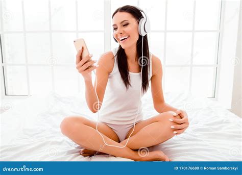Pretty Woman In Headphones Sitting On Bed With Crossed Legs And