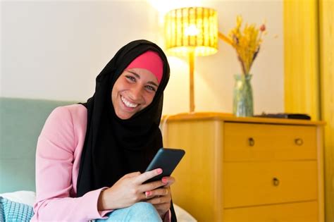 premium photo cheerful muslim woman wearing a hijab using smartphone indoors horizontal side