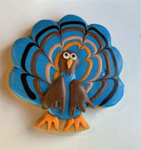 A Cookie Shaped Like A Turkey On A White Table With Blue And Orange Icing