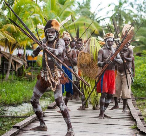 Papuans With A Bow And Arrow Men Of The Papuan Korowai Tribe On A Log