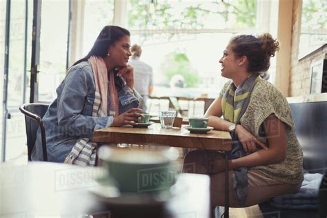 Women Friends Drinking Coffee And Talking At Cafe Table Stock Photo