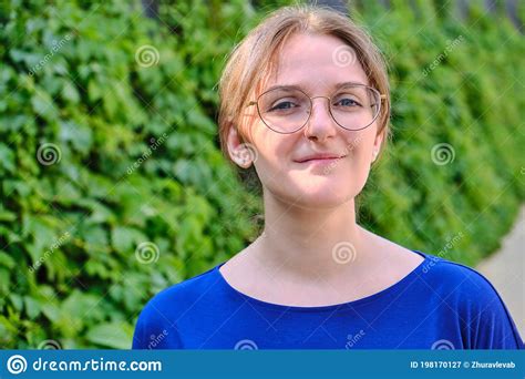 face of a brunette woman wearing glasses and blue clothes close up woman smile in the sun in