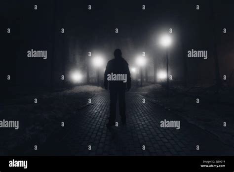 Sad Man Alone Walking Along The Alley In Night Foggy Park Stock Photo