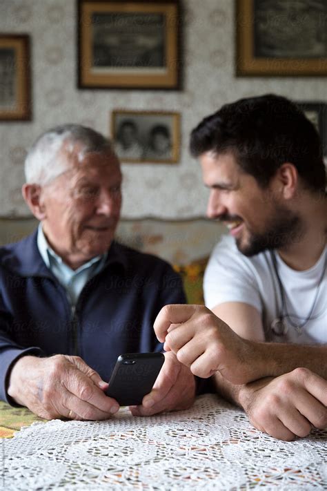 Adult Grandson Explaining To His Granddad How To Use A Smartphone By