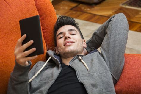 Handsome Young Man At Home Reading With Ebook Reader Stock Image