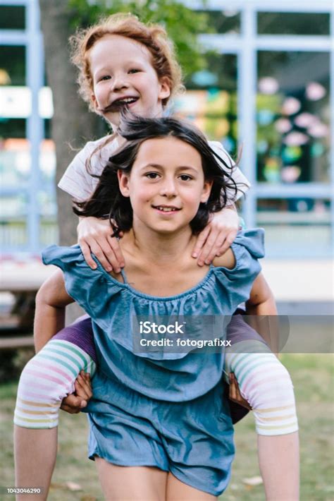 Friendship Two Cute Girls Have Fun With Piggyback In Schoolyard Stock