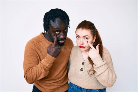 Interracial Couple Wearing Casual Clothes Pointing To The Eye Watching You Gesture Suspicious