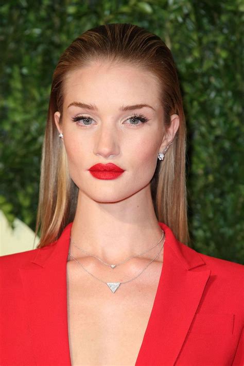 A Woman In A Red Suit With Long Blonde Hair And Bright Lipstick Is