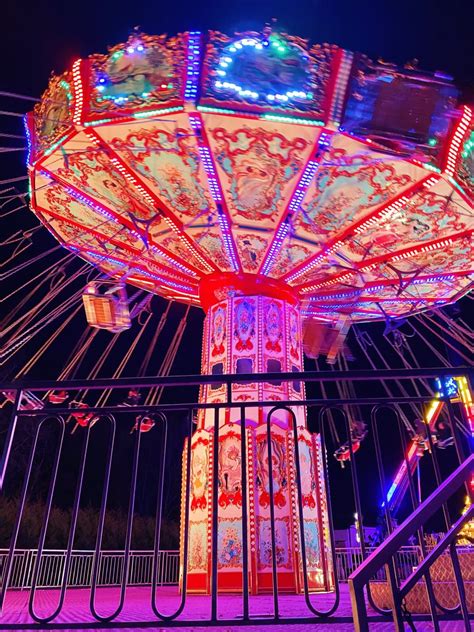 An Illuminated Carnival Ride At Night With Stairs Leading Up To The Top