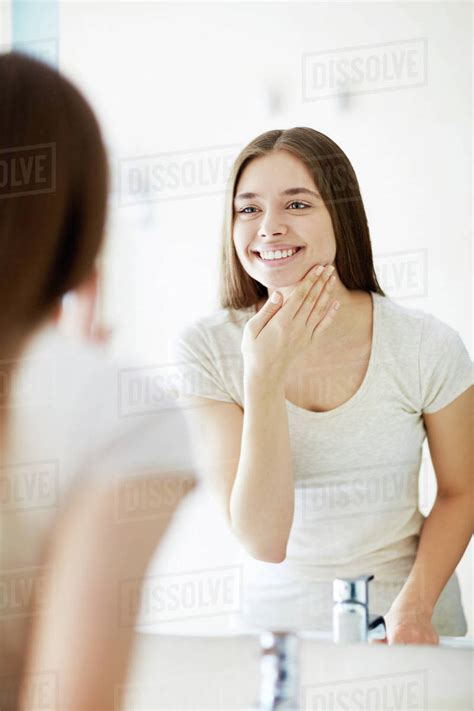 Smiling Young Woman Taking Care Of Skin In Front Of Mirror Stock