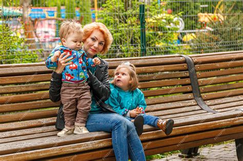Красивая девушка мать с дочерью и сыном в парке сидят на скамейке Премиум Фото