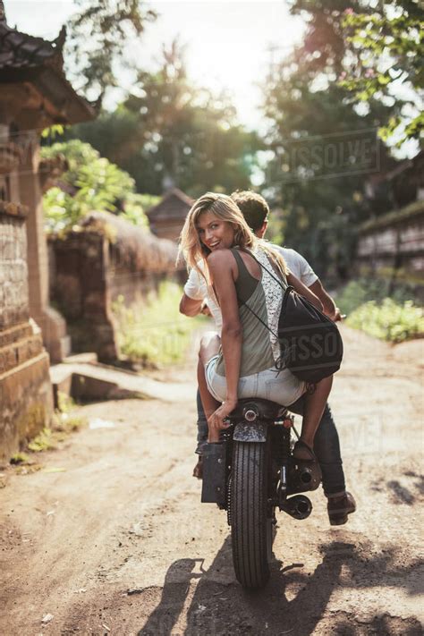 Rear View Shot Of Young Couple Riding Motorcycle On Rural Road