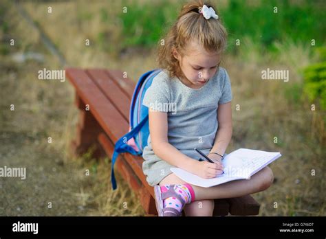 Little School Miss Sits Having Crossed Legs On A Park Bench And