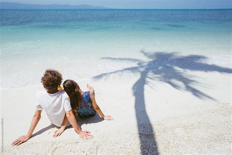 Couple Sitting Together On The Beach Next To Palm Tree Shadow By