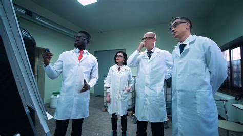 Four scientists in white lab coats standing indoors and discussing ...