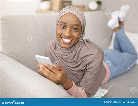 Online Life Smiling Black Woman In Hijab Lying On Sofa With Smartphone