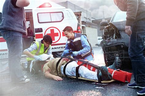 Rescue Workers Tending To Car Accident Victim In Road Stock Photo