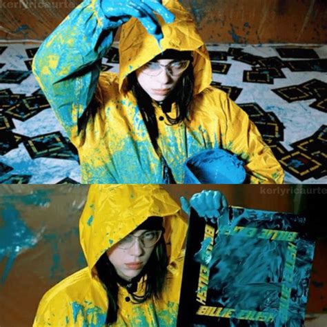 A Woman In Yellow Raincoat Holding Up A Blue And Green Painting On Her Face