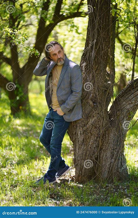A Nice Looking Mature Birded Man In Casual Standing Under Tree On The