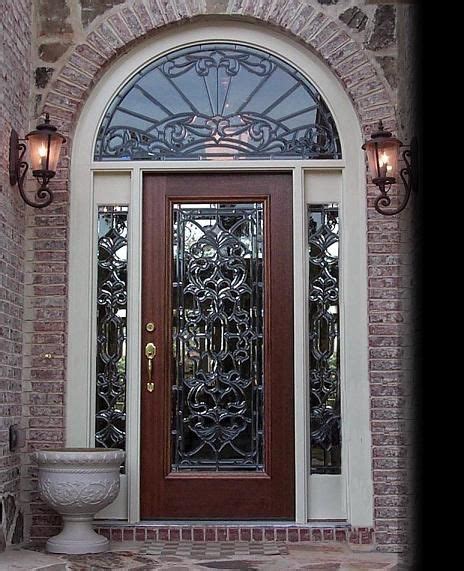 The Front Door Is Decorated With Wrought Ironwork And Glass Panels Along With A Urn