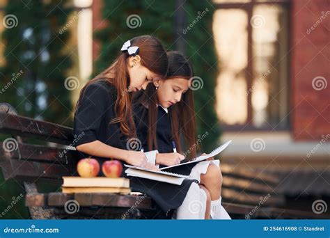 Sitting And Reading Two Schoolgirls Is Outside Together Near School