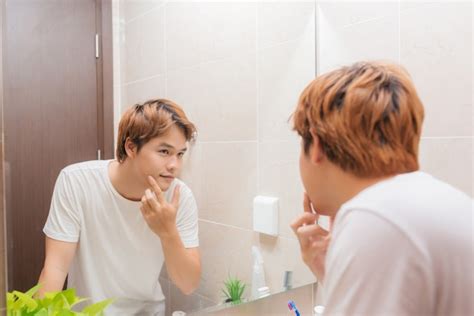 Premium Photo Young Man Standing In Front Of Mirror And Touching His Face