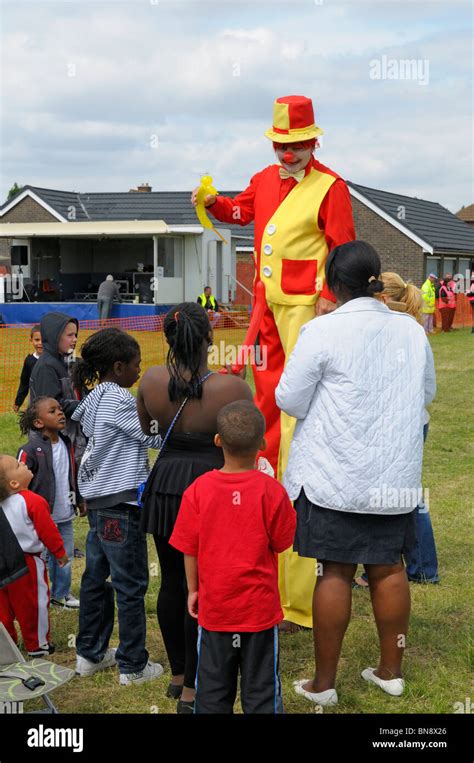 Clown On Stilts At Carnival Showing Children How To Make Balloon