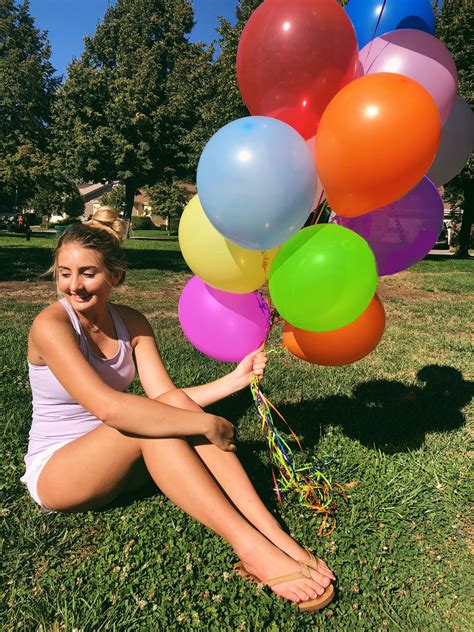 A Woman Sitting In The Grass With Many Balloons