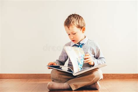 Boy Sitting On The Floor With Reading A Book On His Knees On White