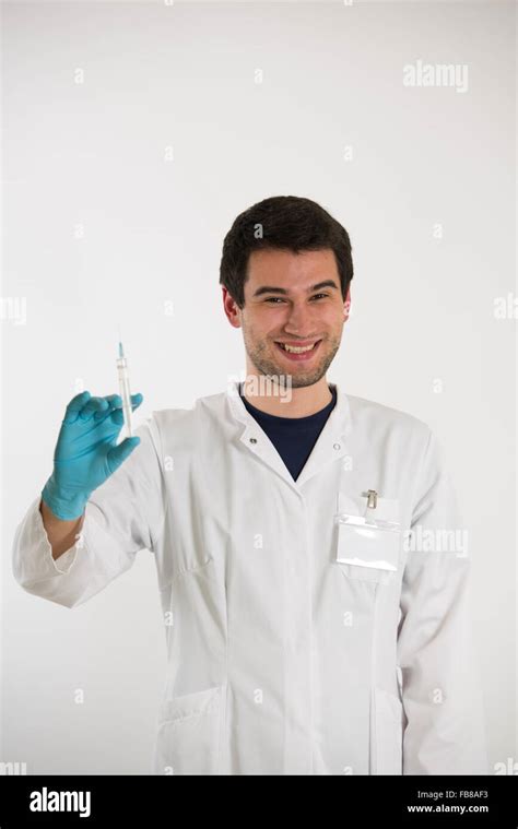Young Male Doctor On White Background Wearing White Coat And Blue Gloves Holds Syringe Stock