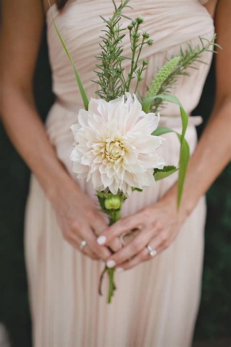 A Woman In A Long Dress Holding A White Flower And Greenery With Her Hands