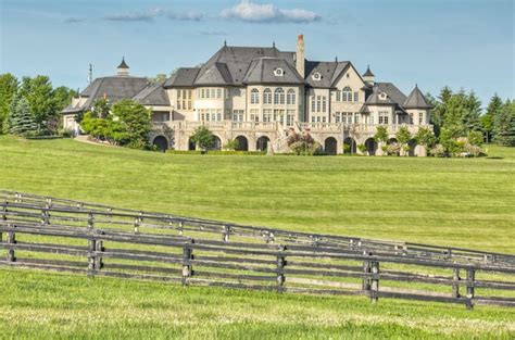 A Large House Sitting On Top Of A Lush Green Field Next To A Wooden Fence