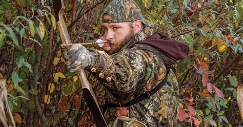 A Man In Camouflage Holding A Bow And Aiming It At The Camera With An Arrow