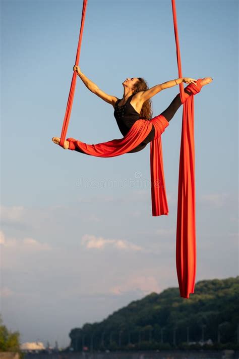 beautiful and flexible female circus artist dancing with aerial silk on a sky background stock