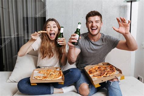 emocionada pareja joven comiendo pizza y bebiendo cerveza mientras están sentados juntos en el