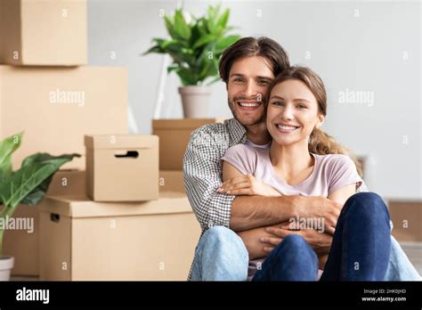 Cheerful Millennial Caucasian Guy Hugging Woman Sit Among Boxes Plants