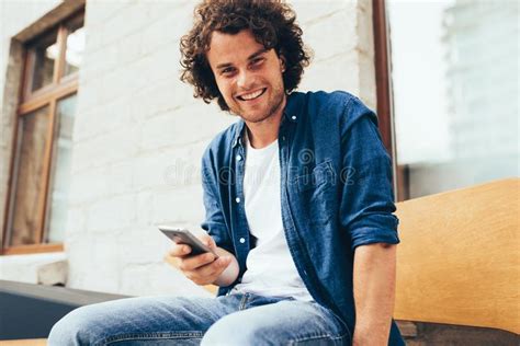 Um Jovem Sorridente Sentado Ao Ar Livre Escrevendo Sms No Celular