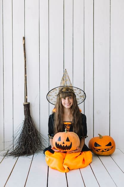 Девушка в костюме хэллоуина сидящая в студии с тыквами и метлой Бесплатно Фото